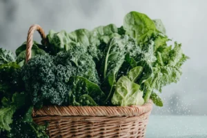 A selection of fresh leafy green vegetables including spinach, kale, and Swiss chard in a woven basket.